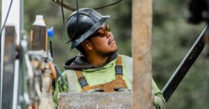 Construction worker in a hard hat and safety glasses inspects a perforated metal panel on a construction site.